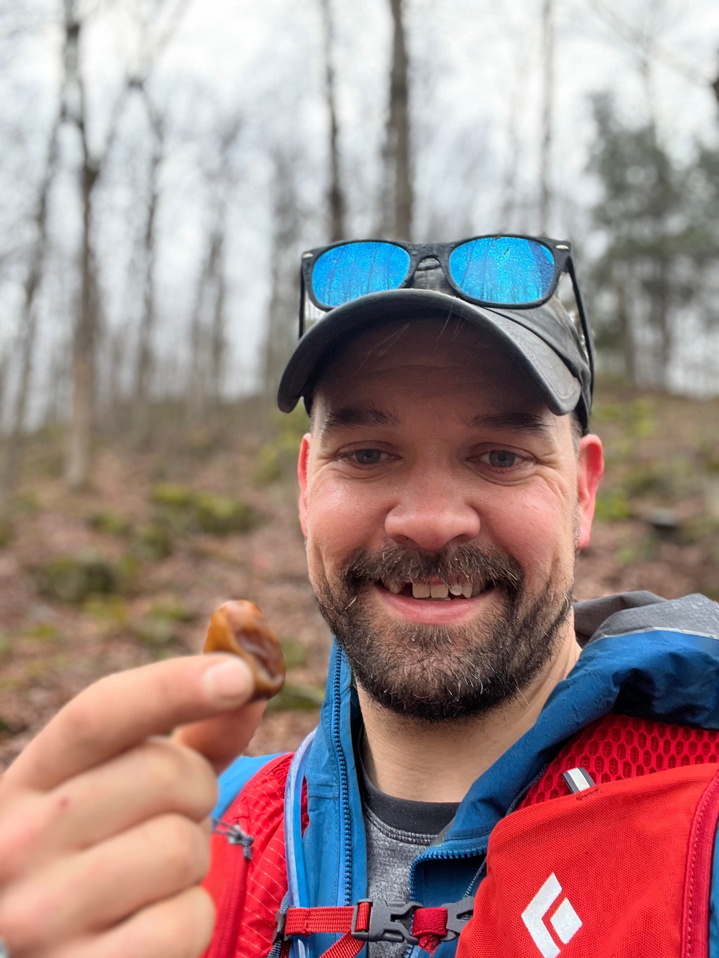 A man smiling and holding a Mighty Mejdool date outdoors, showcasing a natural energy snack for an active lifestyle