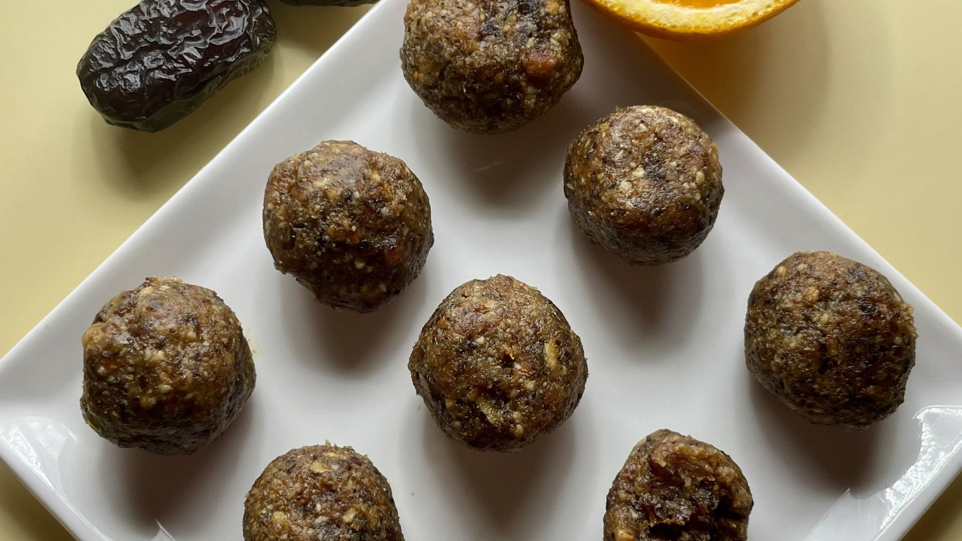 Homemade Safawi date energy bites on a white plate with a whole date and orange slice, a natural pre-run snack for endurance runners