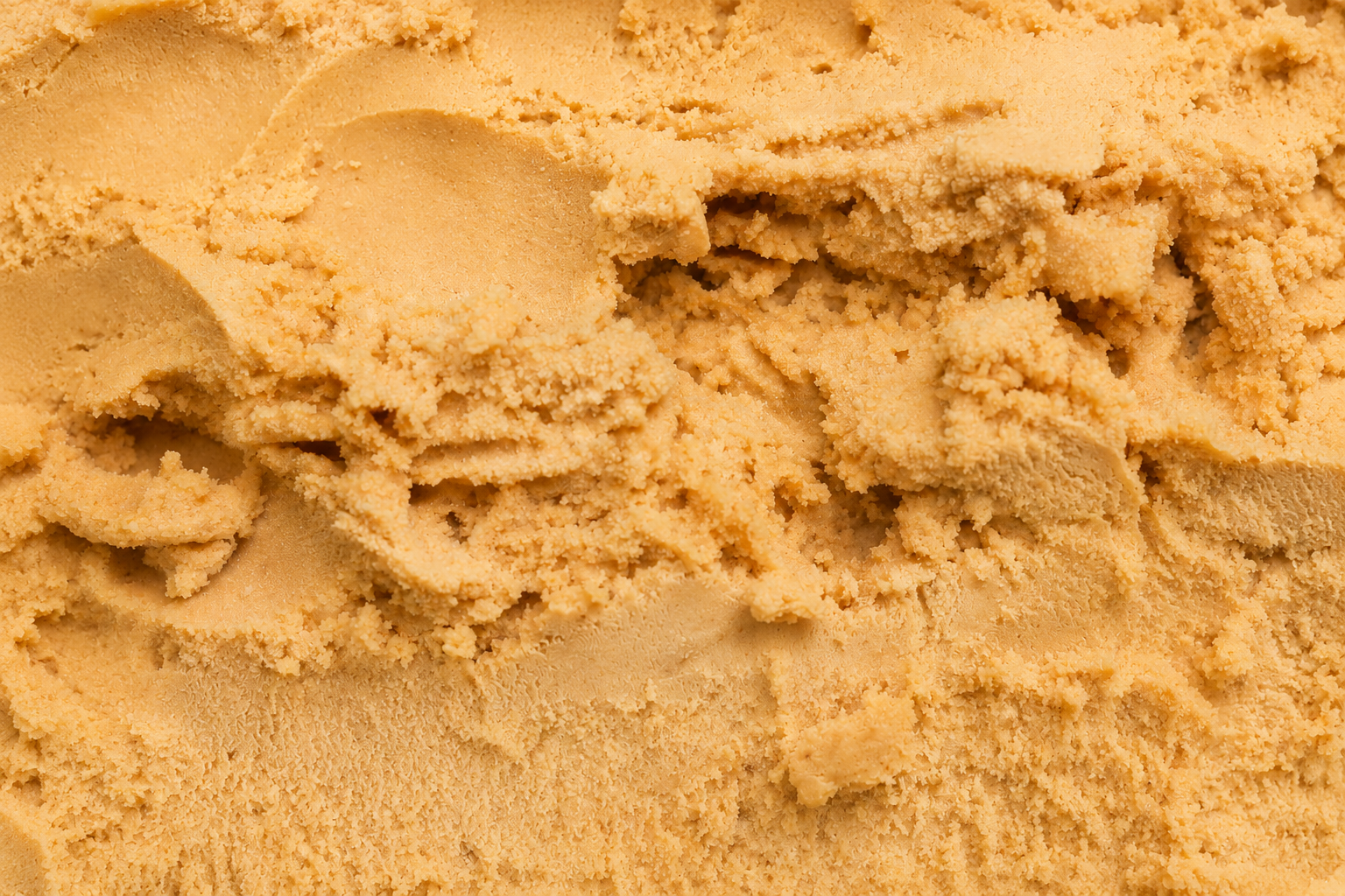 Close-up of homemade Sukkari date ice cream made in a Ninja Creami, showing a creamy caramel-beige texture with soft scoops, ridges, and swirls filling the frame.