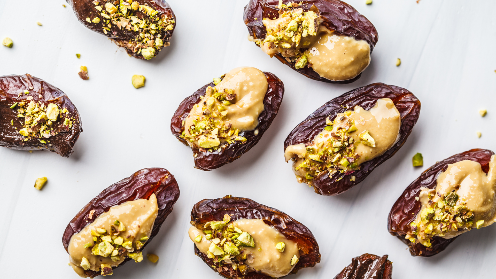 Medjool dates filled with creamy peanut butter and topped with crushed pistachios on a white background.