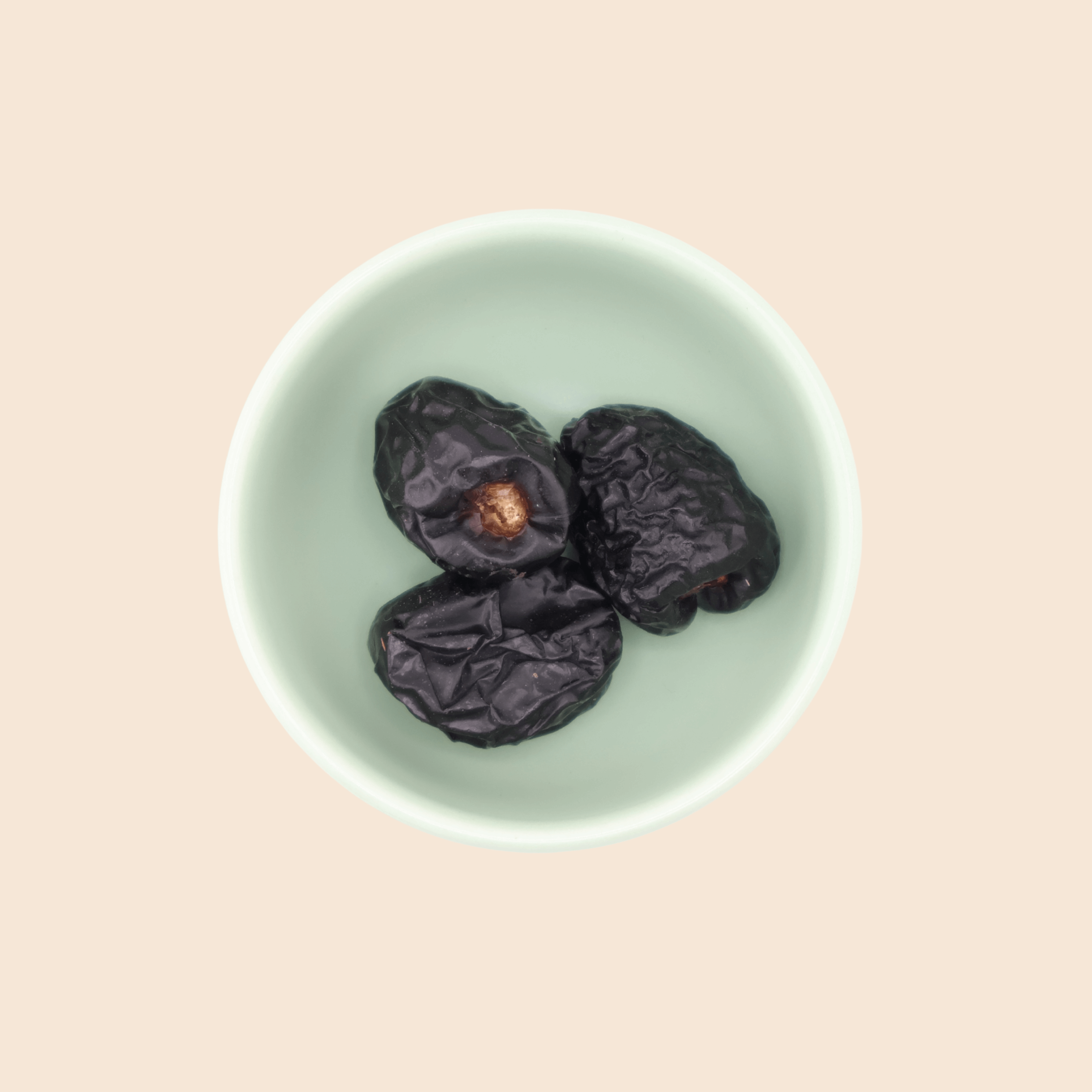 Three Ajwa dates from Mighty Mejdool in a green bowl, showing dark smooth skin and tender texture.