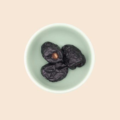 Three Ajwa dates from Mighty Mejdool in a green bowl, showing dark smooth skin and tender texture.