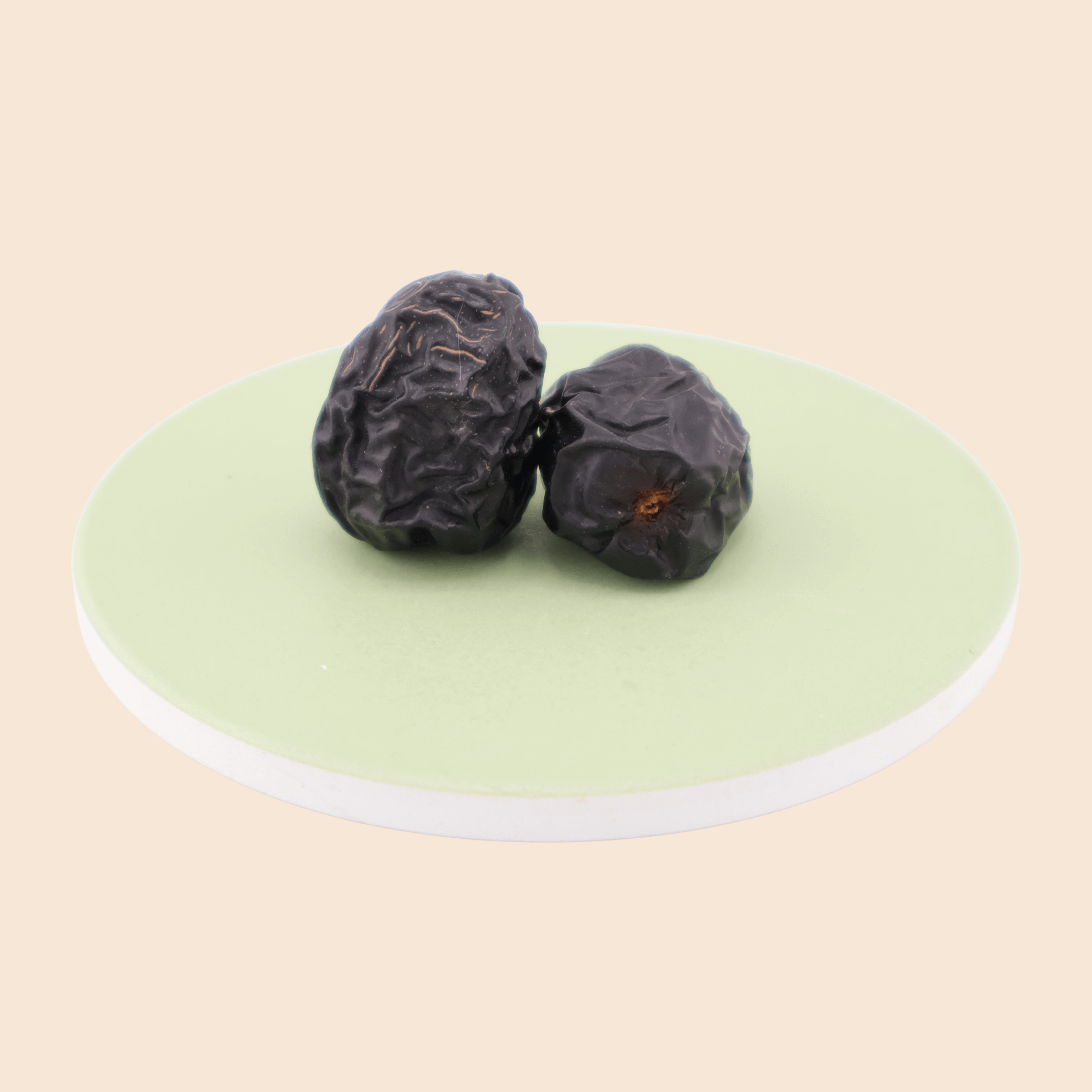 Two Ajwa dates from Mighty Mejdool on a light green plate, showing smooth dark skin and soft texture.