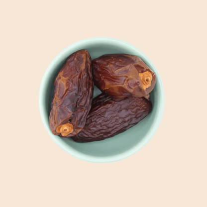 Three large Medjool dates from Mighty Mejdool in a light green bowl, showing deep amber skin and chewy caramel texture.