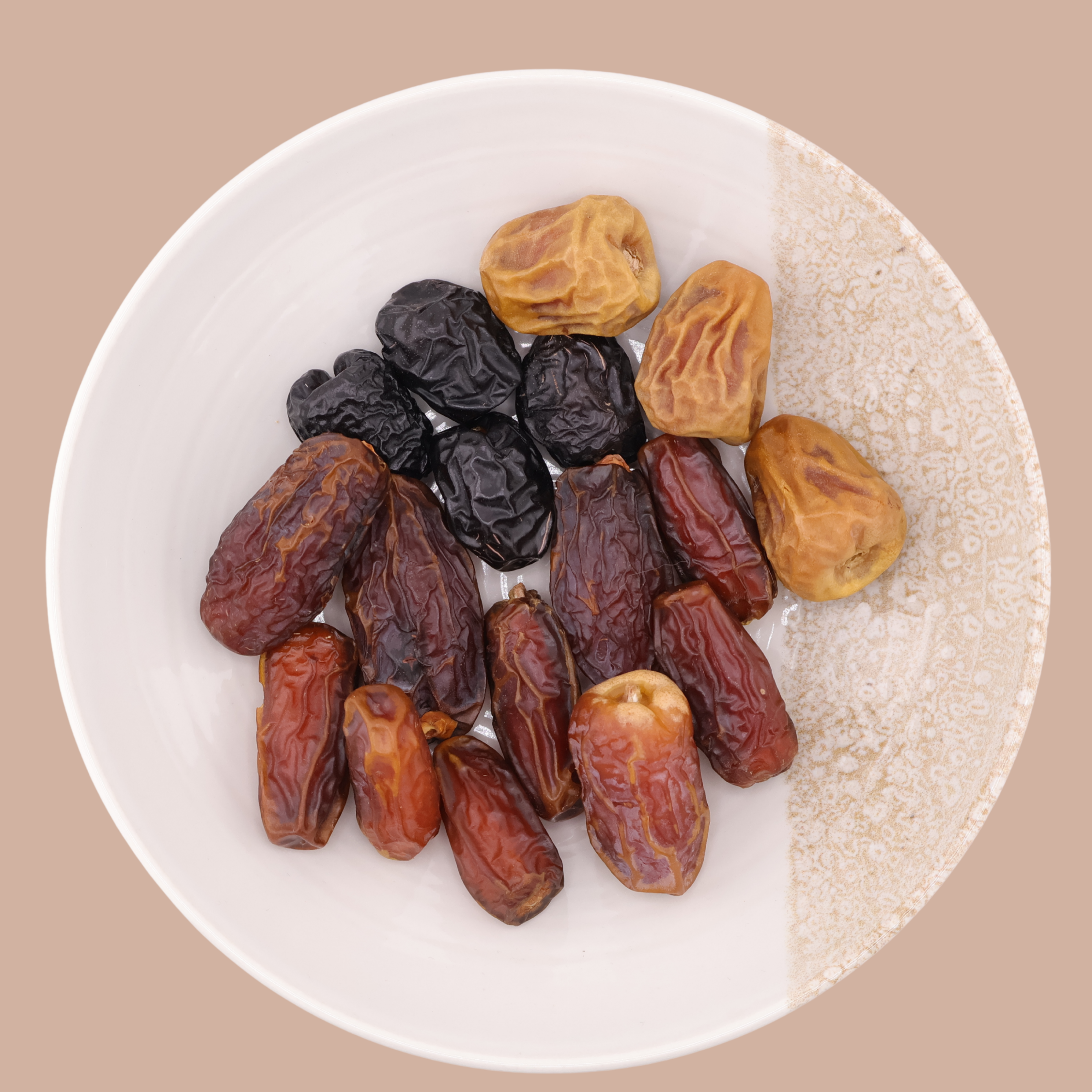 A white bowl showing a mix of premium Mighty Mejdool dates: Sukkari, Ajwa, Sagai, Mabroom, and Medjool. All neatly arranged on a beige background