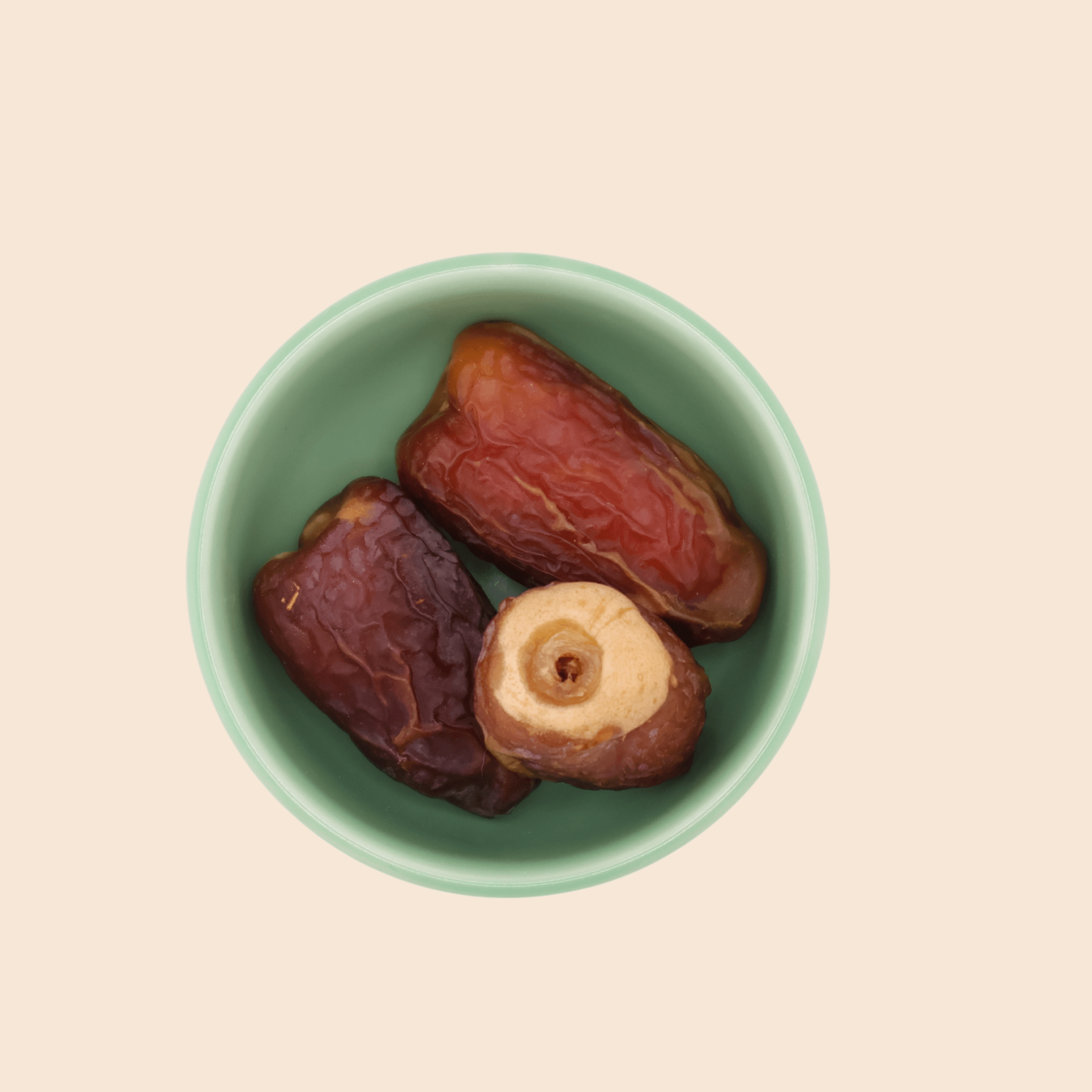 Three Sagai dates from Mighty Mejdool in a green bowl, showing their golden-brown two-tone colour and chewy texture.