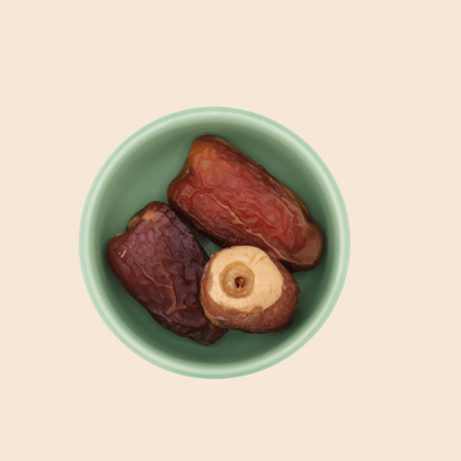 Three Sagai dates from Mighty Mejdool in a green bowl, showing their golden-brown two-tone colour and chewy texture.