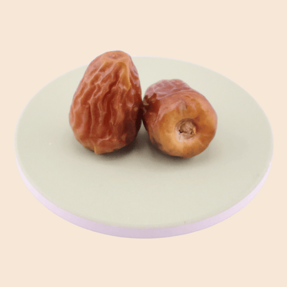 Close-up of two Sukkari Galaxy dates on a coaster, showing soft texture and warm caramel colouring